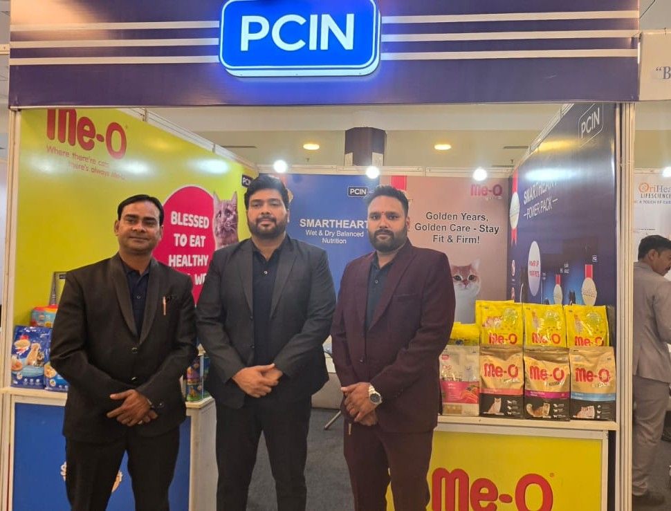 Three professionals standing at PCIN pet nutrition booth displaying Me-O brand products at veterinary conference exhibition